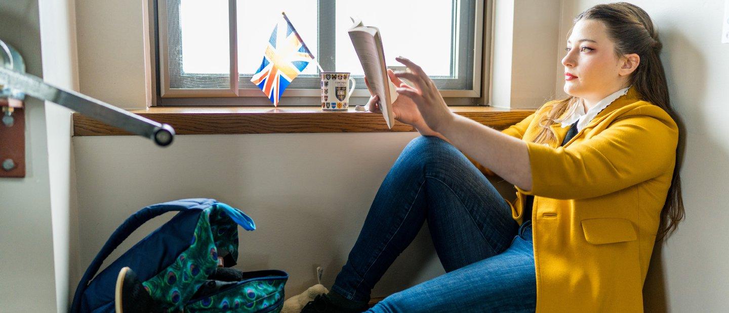 A woman sitting on the floor in a room, reading a book.